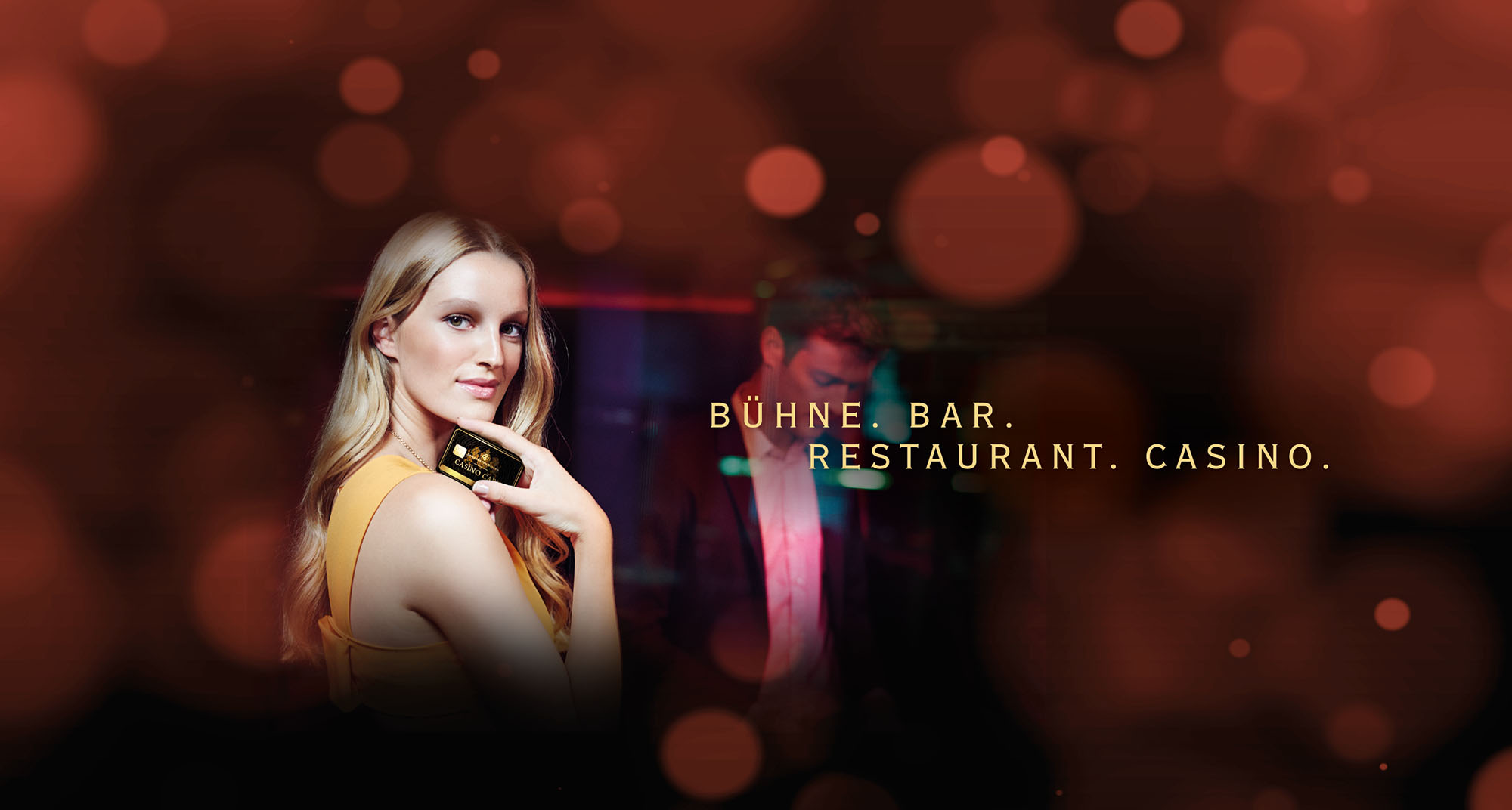 Symbolbild Bühne, Bar, Restaurant, Casino: Dame mit Casino-Card im Vorgrund und Herr im Anzug im Hintergrund