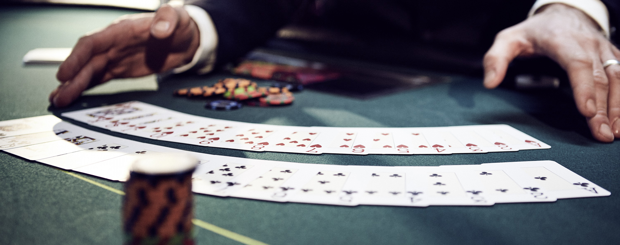 Zwei Hände präsentieren Spielkarten, die in zwei Reihen fächerförmig auf einem Black-Jack-Tisch liegen.